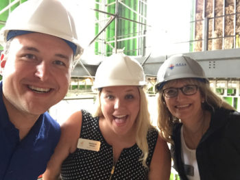 Three people in construction hats inside renovated building smiling for photo