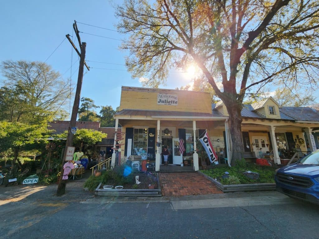 historic downtown street facade with yellow shop behind soaring oak tree with sun shining through - Verna Cora's in Historic Juliette, GA home to Fried Green Tomatoes
