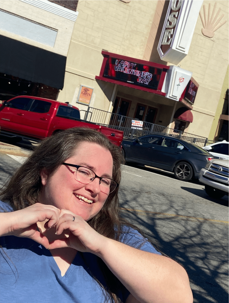 Forsyth CVB Assistant Chelsea Kerr stands on the square in front of the Rose Theater making a heart with her hands